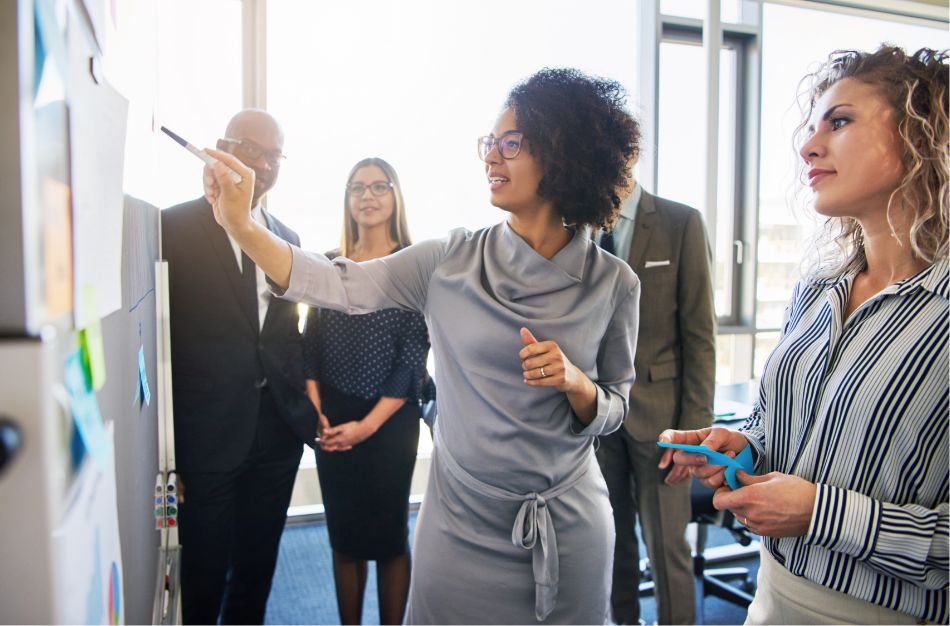 A group of business people discussing strategies around a whiteboard labeled "AI Agents."