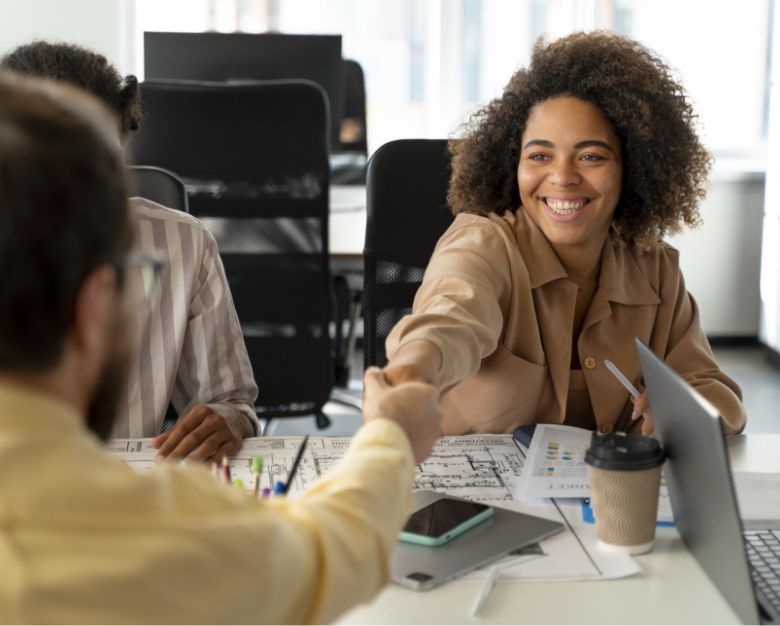 A woman and a man shake hands in an office, symbolizing a professional agreement or collaboration.